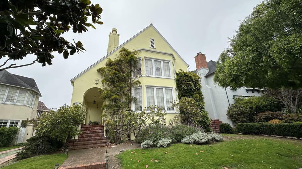 Yellow stucco San Francisco home with a mature climbing vine over its arched entry and an established front garden.