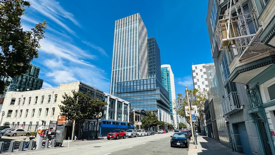 A SoMa street of low buildings running toward a glass tower rising downtown.