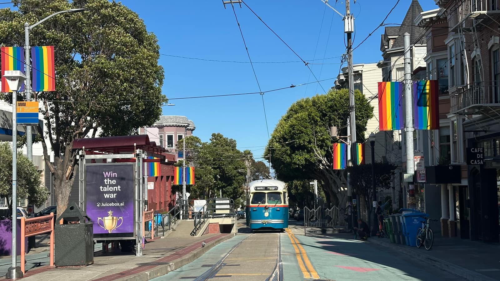Castro Street beneath rainbow flags, a vintage streetcar approaching between Victorian flats and shopfronts.