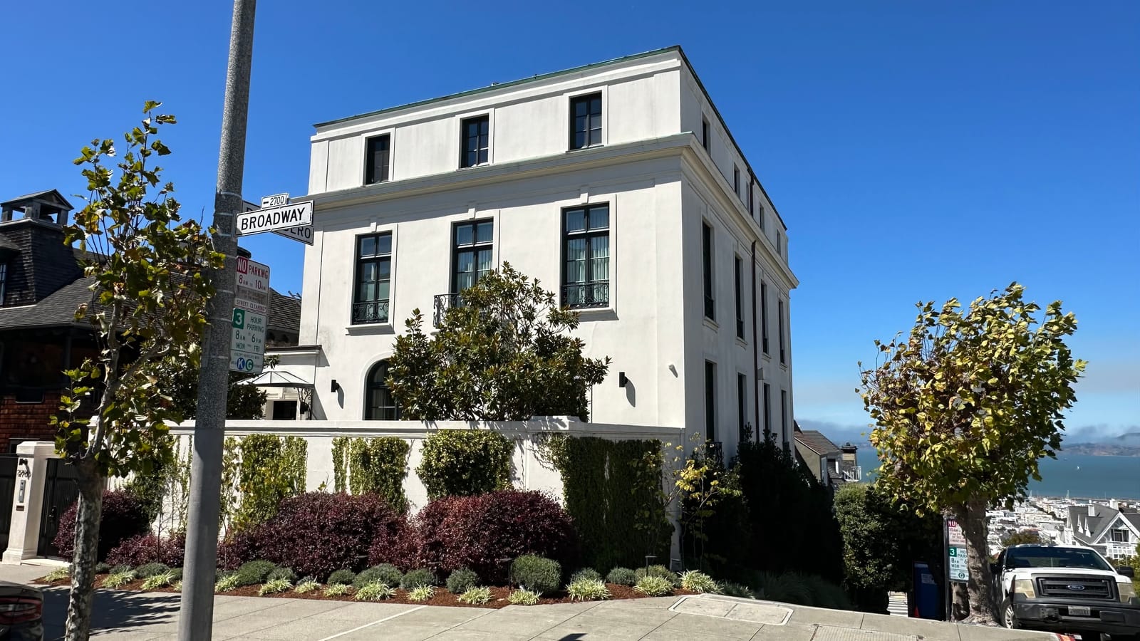 A white contemporary house on the corner of Broadway in Pacific Heights, clipped hedging along the sidewalk and the bay beyond.