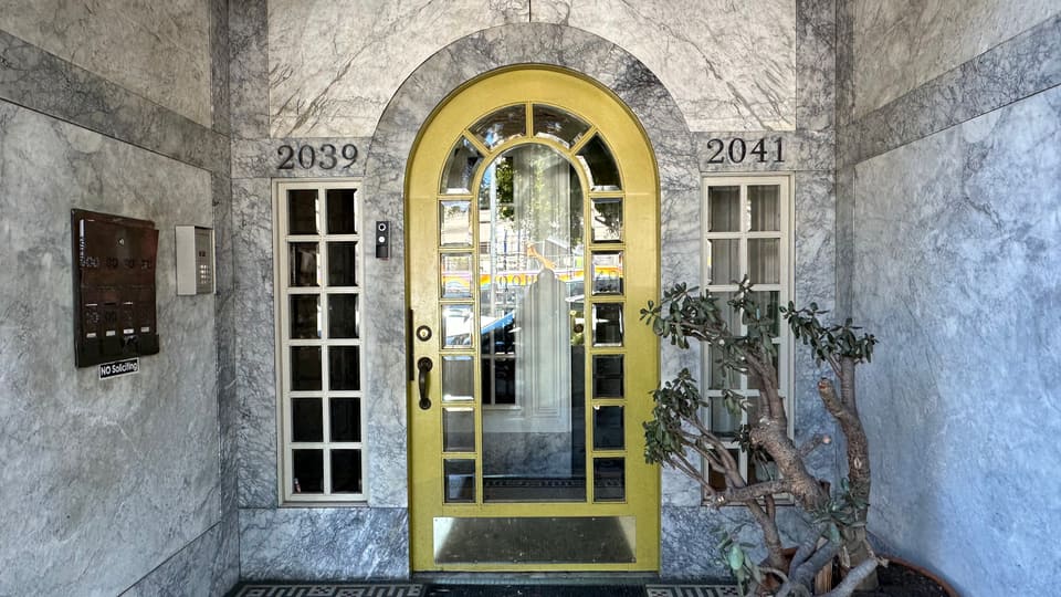 A yellow arched front door set between the street numbers 2039 and 2041, with a shared bank of mailboxes and a buzzer panel on the marble wall beside it.