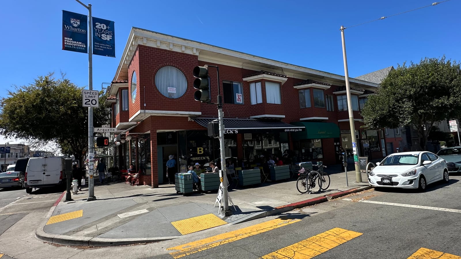 A red-brick commercial corner in the Inner Richmond, shopfronts at street level and a painted crosswalk in the foreground.