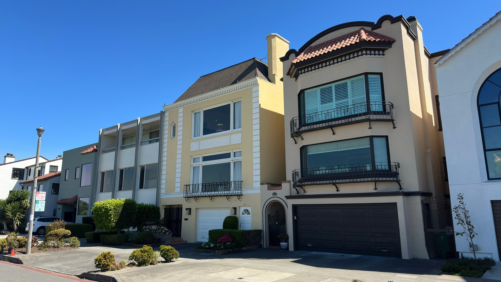 Marina-style homes in cream and pale yellow, garages at street level and bay windows above, on a sunlit block.