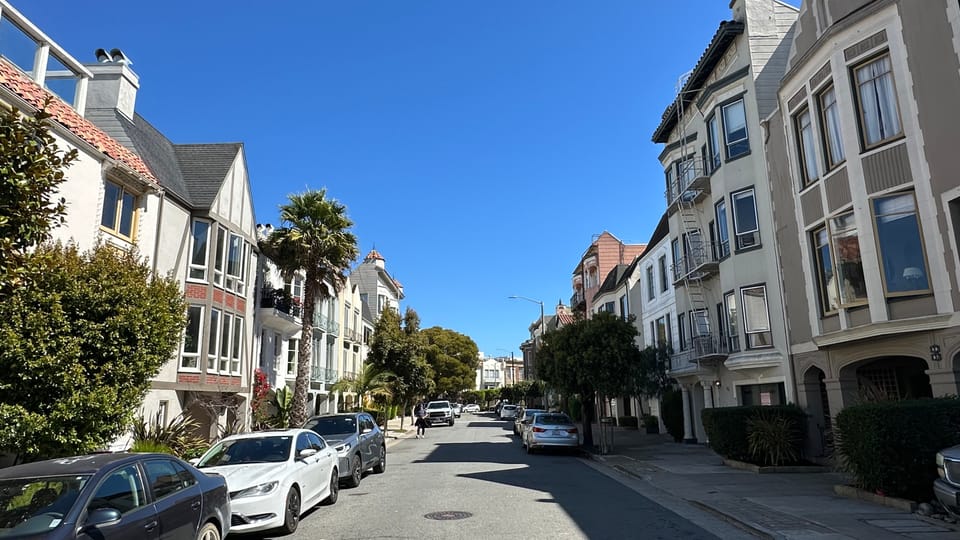 A Marina district street of white and cream homes sloping toward the bay, palms along the sidewalk under a clear sky.