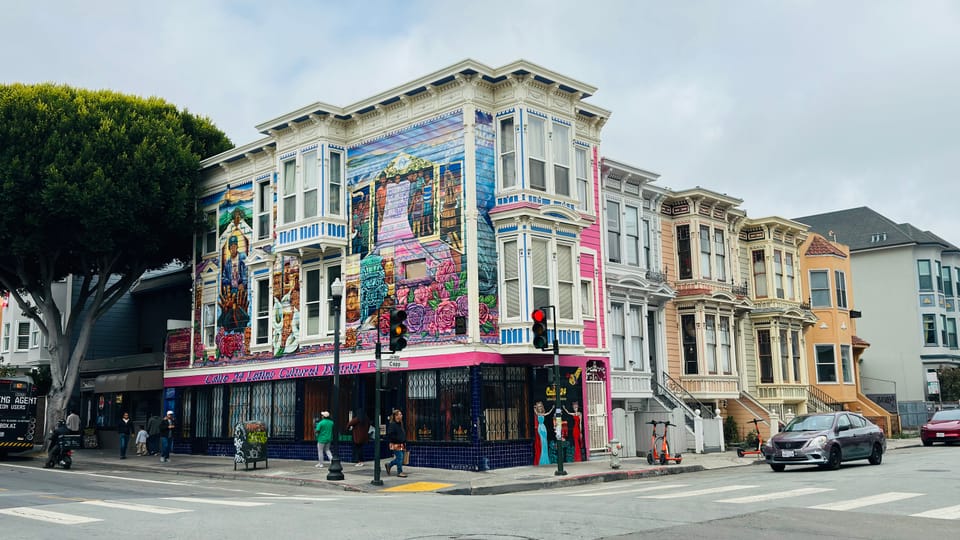 A muralled corner Victorian on Valencia Street in San Francisco's Mission District, with a row of Victorian facades receding up the block.