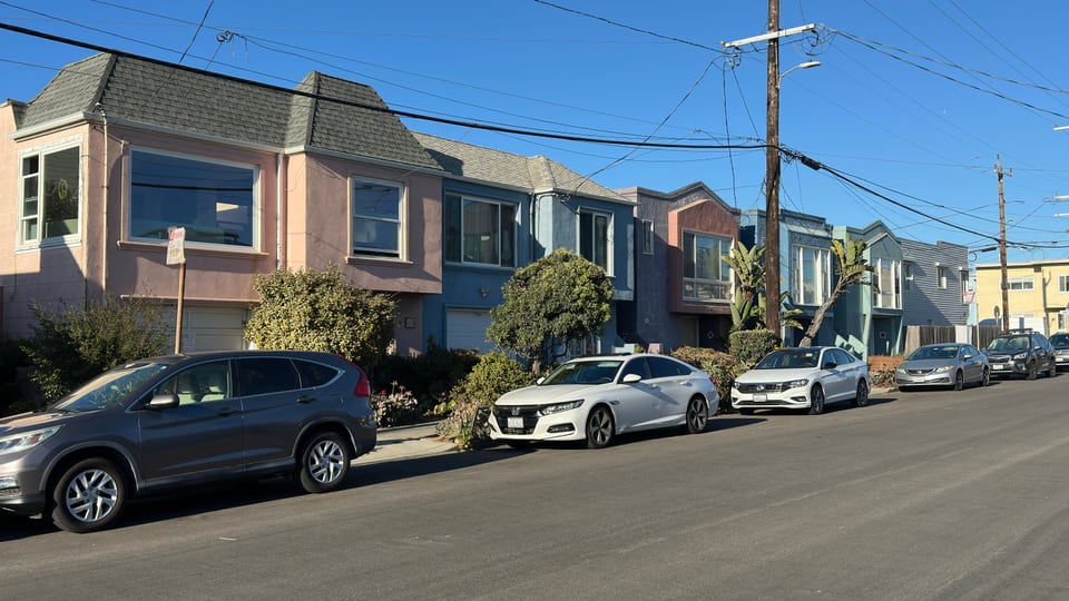 A sunlit row of pastel stucco homes with bay windows and ground-floor garages on an Outer Sunset block.