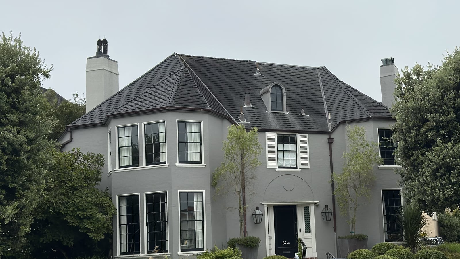 Grey slate-roofed Sea Cliff estate with arched dormer, framed by mature olive trees on a quiet corner.