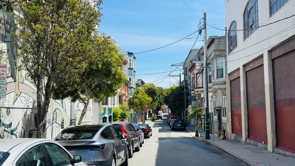 A quiet SoMa block of garages and low flats climbing away from the camera, street trees along one side.