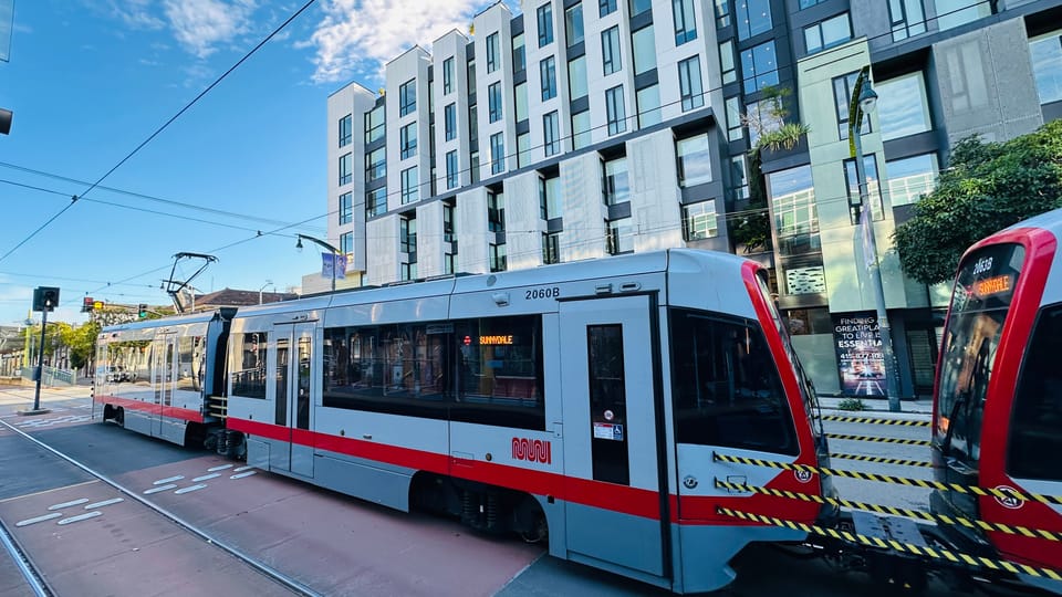 A Muni light-rail train on its own right of way beside new apartment blocks near UCSF Mission Bay.