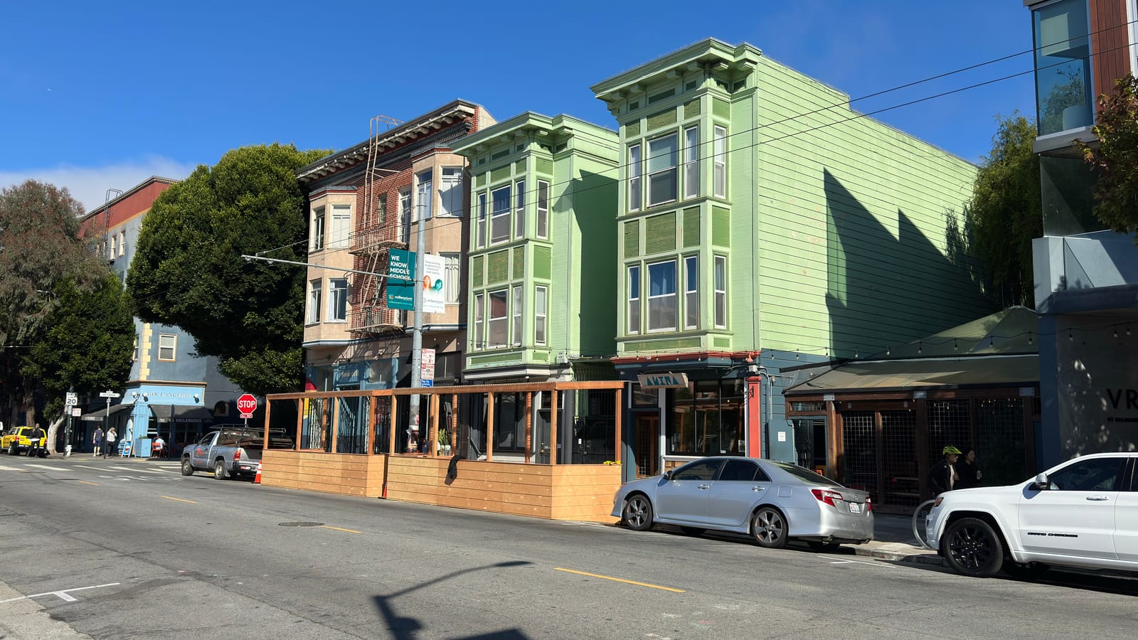 Green and yellow Victorian storefronts along Hayes Street, with a sidewalk parklet and cafe seating under a clear sky.