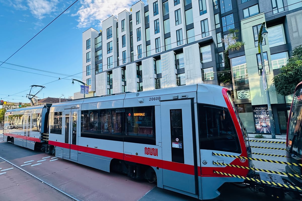 A Muni T-Third light rail train on Third Street in San Francisco's Mission Bay, with the neighborhood's mid-rise apartment buildings behind.