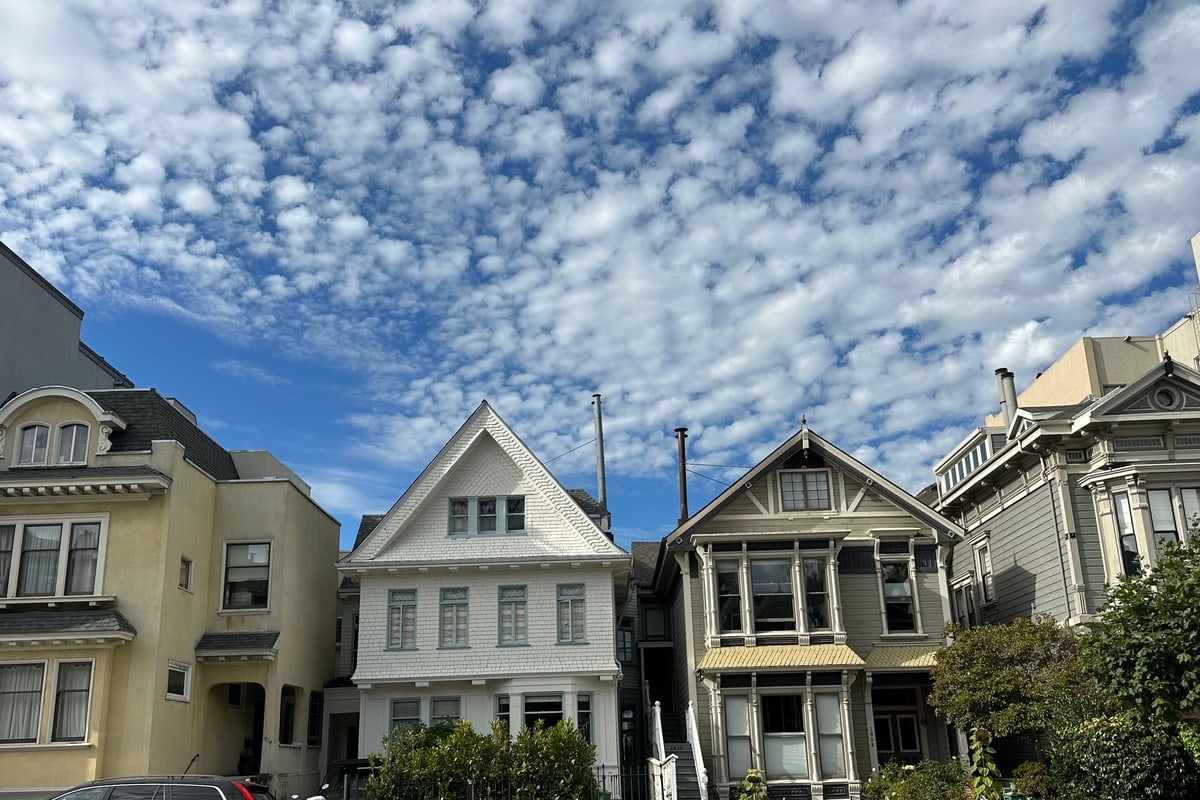 A row of pastel Victorian and Edwardian houses on a Pacific Heights hillside street in San Francisco, beneath a mackerel sky.