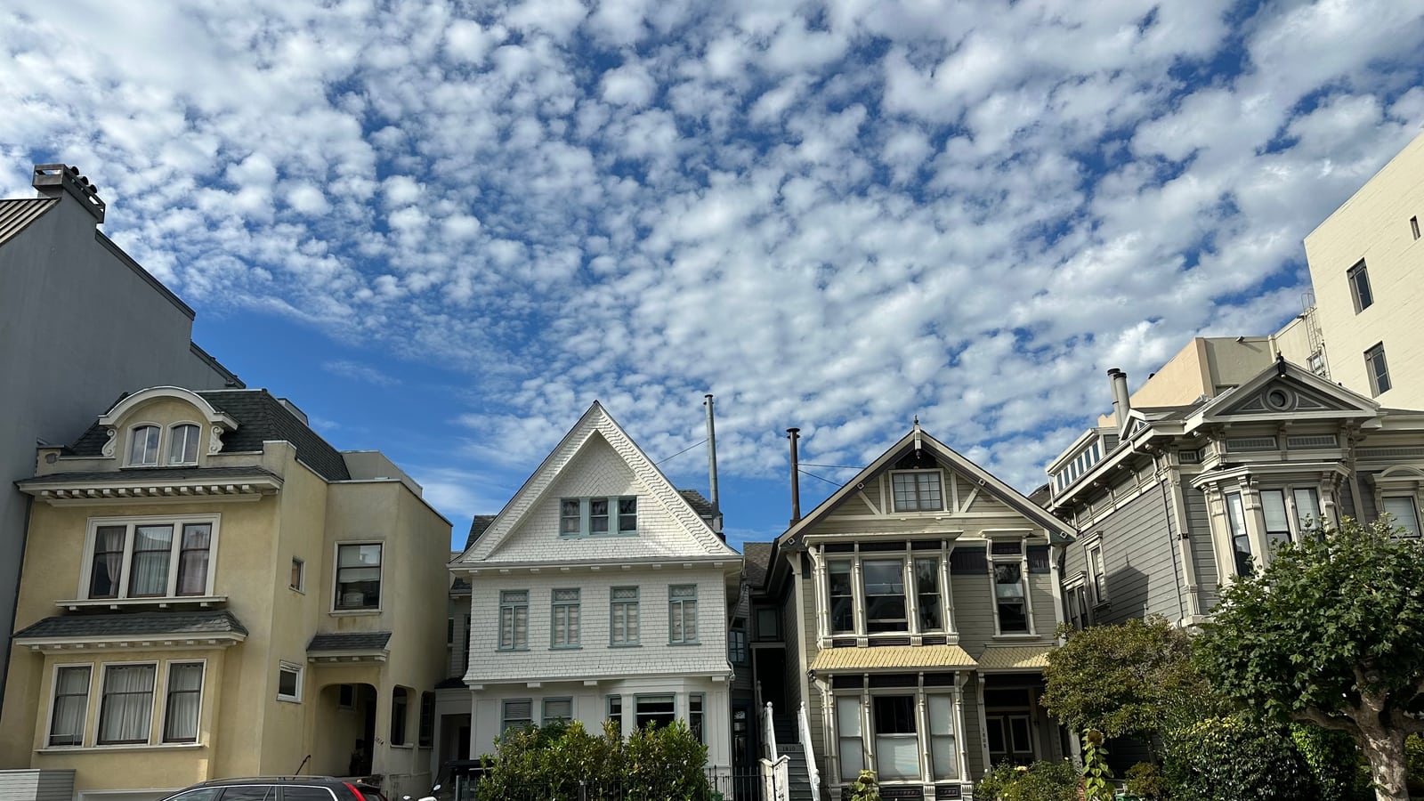 A row of pastel Victorian houses climbing a Pacific Heights block under a mackerel sky.