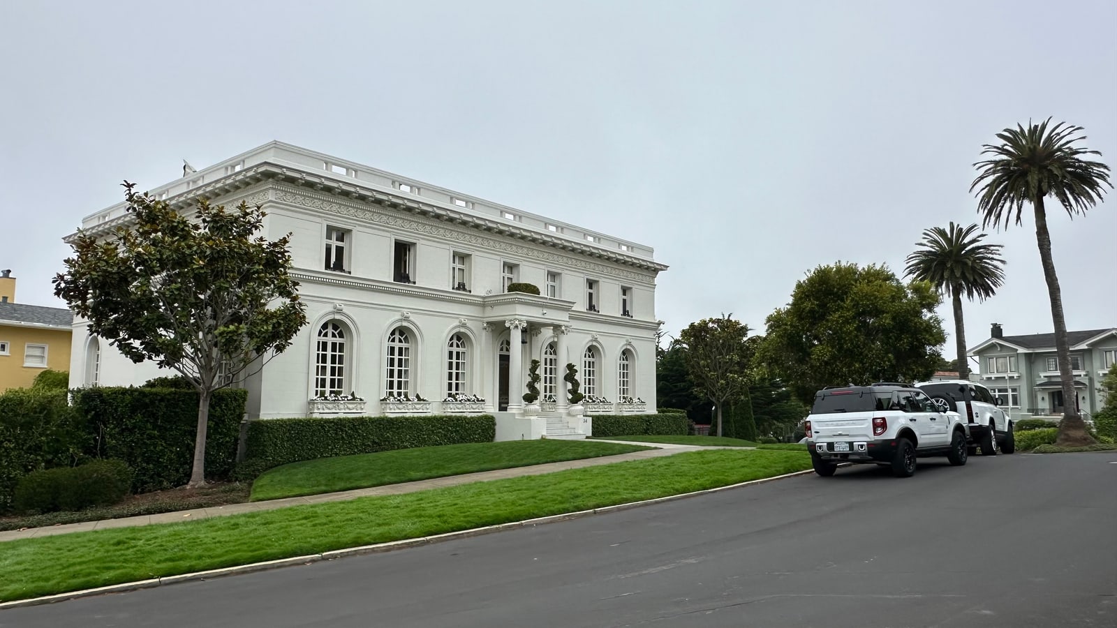 A white neoclassical mansion set behind a clipped lawn on a Presidio Heights street, palms rising beside its columned entry.