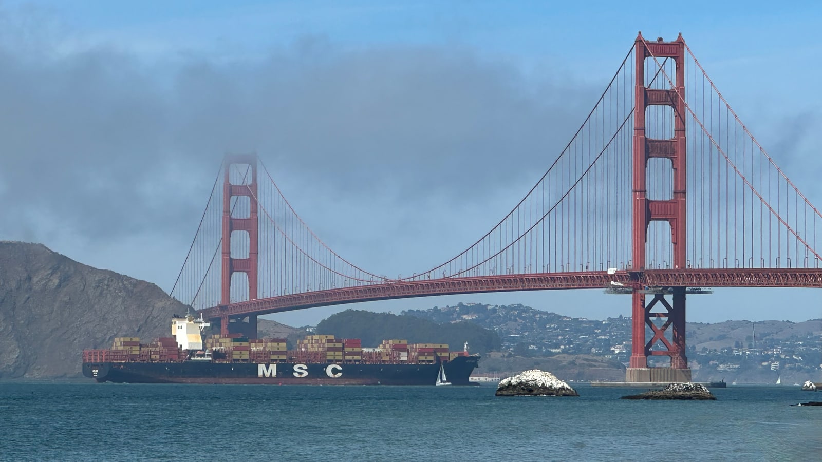 The Golden Gate Bridge seen from Baker Beach at the western edge of Sea Cliff, San Francisco, a container ship passing beneath and the Marin Headlands behind.